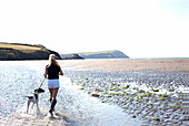 Woman walking dog on beach, Wales, UK