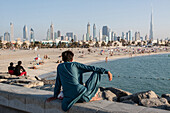 Man looking at the beach and the skyline of sheikh zayed road with the financial center and downtown dubai dominatd by the burj khalifa tower, once known as burj dubai, dubai, united arab emirates, middle east