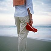 Woman Standing on Beach Holding Flip Flops