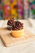 Two Cupcakes with Chocolate Icing on Wood Cutting Board