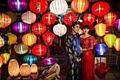 Vietnamese couple poses between the colorful lanterns of a lantern shop in Hoi An, Vietnam