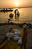 Silhouette of a man washing cloths in the Ganges river at sunrise white boats pass and the sun is rising in the background, Varanasi, India