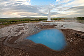 The surreal blue lake in the Strokkur  geyser area in the moment of eruption of the geyser at sunset