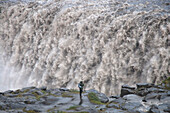 A photographer watches the mighty Dettifoss waterfall falling into the canyon below, Iceland