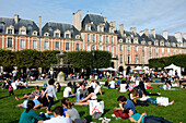 Autumn sun, people on lawns, public garden, Place des Vosges, Paris, France