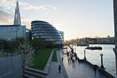 'Pedestrians and buildings along the promenade beside River Thames; London, England'