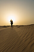 'Man in smart suit making phone call on top of sand dune at dusk; Dubai, United Arab Emirates'