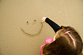 A Girl Draws A Happy Face In The Sand