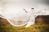 'A Bride Standing In A Field And Holding Out Her Veil In The Wind; Ontario, Canada'