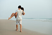 'A Man Carrying A Woman Down Los Lances Beach In Costa De La Luz; Tarifa, Cadiz, Andalusia, Spain'