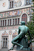 'Bronze Male Statue With Colorfully Painted Buildings In The Background; Lindau, Germany'