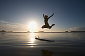 'Silhouette Of Female Surfer Jumping For Joy; Chesterman Beach Tofino Vancouver Island British Columbia Canada'