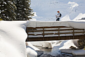 'Female Snowshoeing On Bridge Over Creek; Waterton Alberta Canada'