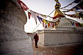 'A Man Walking Amongst The Buildings With Prayer Flags Hanging Above; Kathmandu, Nepal'