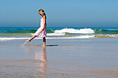 Young Woman Walking Along The Beach Kicking Up Water