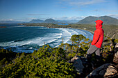 'A Man Wearing A Red Jacket Looks Out At The View Of Cox Bay Near Tofino; British Columbia, Canada'