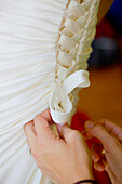 'Hands Fastening The Laces On The Back Of A Bride's Gown; Vancouver, British Columbia, Canada'