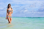 'A Woman Standing In The Ocean Wearing A Colourful Bikini And Sunglasses; Punta Cana, La Altagracia, Dominican Republic'