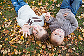 'Portrait of two young boys laying on fallen leaves in autumn colours;St. albert alberta canada'