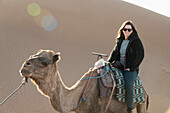 'A woman riding a camel at the sand dunes;Souss-massa-draa morocco'