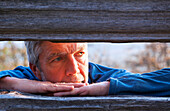'A man views the sunset through fence boards on Mount Tzouhalem on Vancouver Island; British Columbia, Canada'