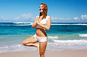 'A young woman does yoga on the beach; Kauai, Hawaii, United States of America'