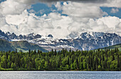 'Mt McKinley peaking through the clouds behind snowy rocky foothills of the Alaska range with Byers lake in the foreground, Denali State Park; Alaska, United States of America'