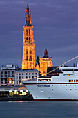 Cruise ship MS Deutschland (Reederei Peter Deilmann) moored along the Scheldt river with Cathedral of Our Lady church tower at dusk, Antwerp, Flemish Region, Belgium