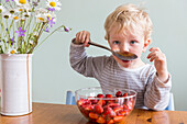 Junge (3 Jahre) isst Erdbeeren mit einem großen Löffel, Leipzig, Sachsen, Deutschland