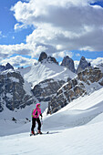 Frau auf Skitour steigt zum Hochebenkofel auf, Schwabenalpenkopf und Drei Zinnen im Hintergrund, Sextener Dolomiten, Südtirol, Italien