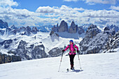 Frau auf Skitour steigt zum Hochebenkofel auf, Paternkofel, Drei Zinnen und Schwalbenkofel im Hintergrund, Sextener Dolomiten, Südtirol, Italien