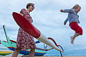 Mother and son playing at the beach, boy jumping from a boat, traditional fisherboat, flying, little boy 3 years old, western family, family travel in Asia, parental leave, MR, Sanur, Bali, Indonesia