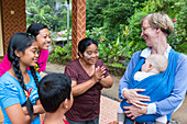Balinesische Familie bewundert deutsches Baby, im Tragetuch der Mutter, lachen, Mädchen 5 Monate alt, Kontakt mit Einheimischen, Elternzeit in Asien, Europäer, Deutsche, Westler, Familie, MR, Munduk, Bali, Indonesien