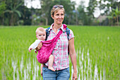 Mother with her baby, baby sling, wrap, in a rice field, paddy, smile, countryside, family travel in Asia, parental leave, German, European, MR, Tetebatu, Lombok, Indonesia