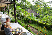 Mutter und Sohn beim Frühstück auf der Terrasse eines Ferienbungalows, Tetebatu, Lombok, Indonesien
