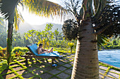 Father and daughter at swimming pool, baby, girl 5 months old, sunbed, lounger, palm trees, evening sun, playing, mountains, hotel, Balinese holiday resort, family travel in Asia, parental leave, German, European, MR, Sidemen, Bali, Indonesia
