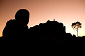 Schattenriss der Devil's Marbles Felsformation mit Baum und Mensch auf Felsen im Dämmerlicht bei Sonnenaufgang, Devils Marbles Conservation Reserve, nahe Wauchope, Northern Territory, Australien