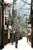 Ein Mann läuft entlang einer fast leeren Straße mit unzähligen Stromleitungen zwischen den Masten, Kyoto, Region Kansai, Japan