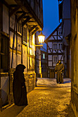 Two people wearing traditional coats meet under a street lamp in a small alley called Paradiesgasse with half-timbered houses at dusk, Bad Wildungen, Hesse, Germany, Europe