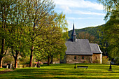 Frühgotische Kirche von Frebershausen, Blick über den alten Friedhof mit großen grünbelaubten Bäumen im Nationalpark Kellerwald-Edersee, Frebershausen, Nordhessen, Hessen, Deutschland, Europa