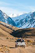 Off-road vehicle passing Monte Desert, snow-covered Andes in background, Las Lenas, Mendoza, Cuyo, Argentinia