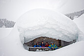 Four skiers in front of a snow-covered cabin, Corvara, South Tyrol, Italy