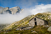 An old alpine cottage, under wild peaks and clouds, Piedmont, Gran Paradiso National Park