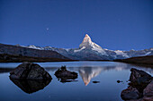 The Matterhorn colossus reflecting in the still water of Lake Stellisee in a clear night. This mirror is just one of the many little lakes spotting the Zermatt heights, famous Swiss resort, Zermatt, Canton of Valais, Switzerland.