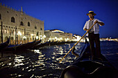 A gondolier navigates canals in Venice, Italy, at night.