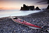 Red sea kayak lying on a pebble beach as the setting sun silhouettes sea stacks on the horizon, Ruby Beach, Olympic National Park, Washington, USA, 7 October 2008