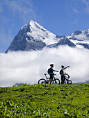 Two mountain bikers are resting near the village of Murren, during a long bike ride in the Bernese Oberland. In the background the famous Eiger mountain.  The Eiger region in the Swiss Bernese Oberland is a Mekka for mountain bikers with almost 100 kilome