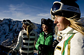 Sue Larson, Amber Gale and Caitlin Phillips looking into the sunset light with skis on top of a mountain, Alta Utah