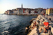 Holidaymakers enjoy a lazy afternoon's fishing in the outer harbour of Rovinj Rovigno., Church of S. Eufemia stands at the top of the hill in the centre of town