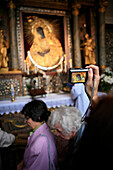 'A woman takes a photograph of a gilded icon of The Blessed Virgin Mary Mother of Mercy as worshippers file past. The painting is the centerpiece of the Gate of Dawn Lithuanian: Au_ros¡ros Vartai, Polish: Ostra Brama, Chapel in Vilnius and has religious a